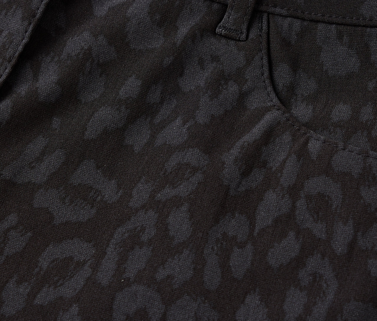 Egy fekete, leopárdmintás nadrág részletének közeli felvétele, beleértve a gombot és a zsebet.