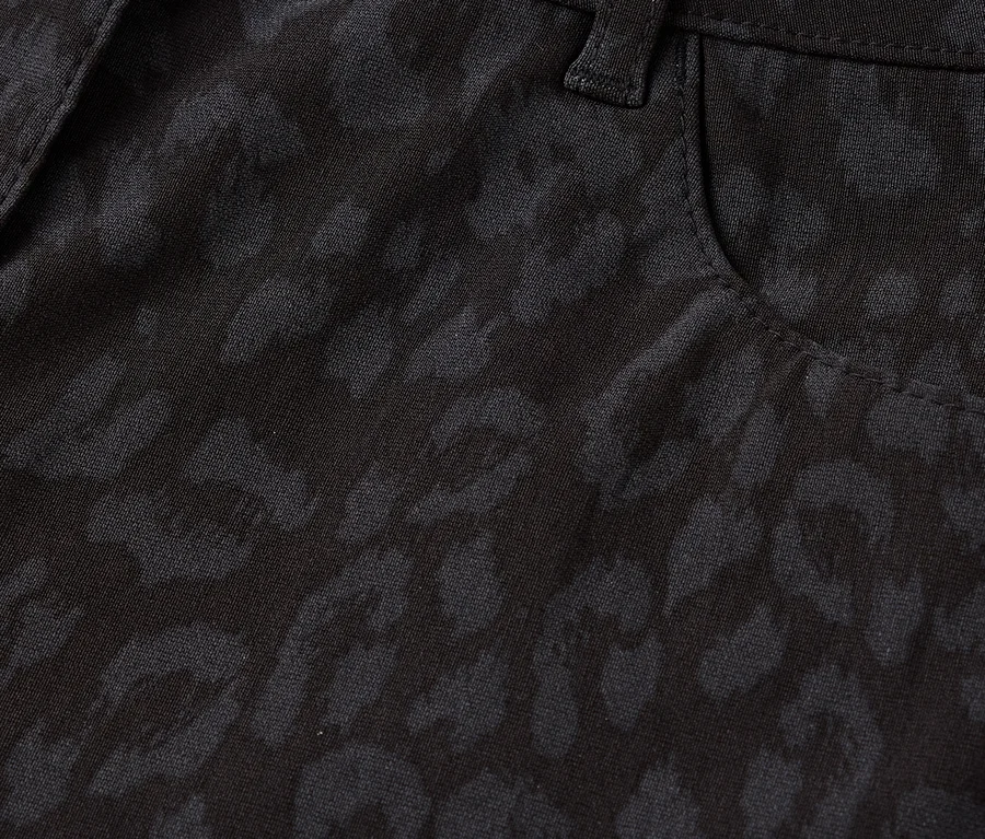 Egy fekete, leopárdmintás nadrág részletének közeli felvétele, beleértve a gombot és a zsebet.