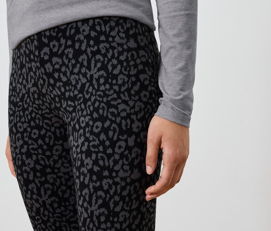 Egy fekete, szürke állatmintás leggingset és szürke, hosszú ujjú inget viselő személy részletfotója.