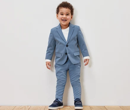 Mosolygó kisfiú kék kisfiú zakóban és chino nadrágban.