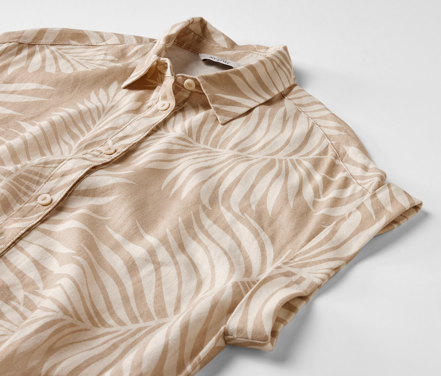 Közelkép egy nyomott mintás lenvászon ruháról, rövid ujjakkal és gombokkal.