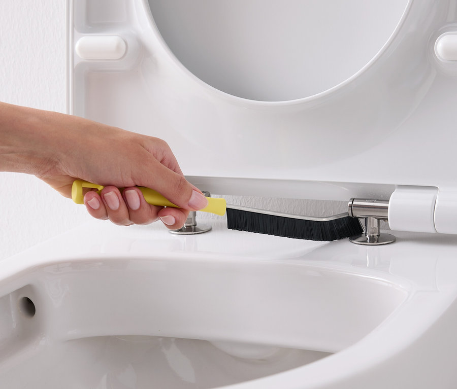 Egy kéz egy sárga kefével tisztít egy fehér WC-ülőkét.