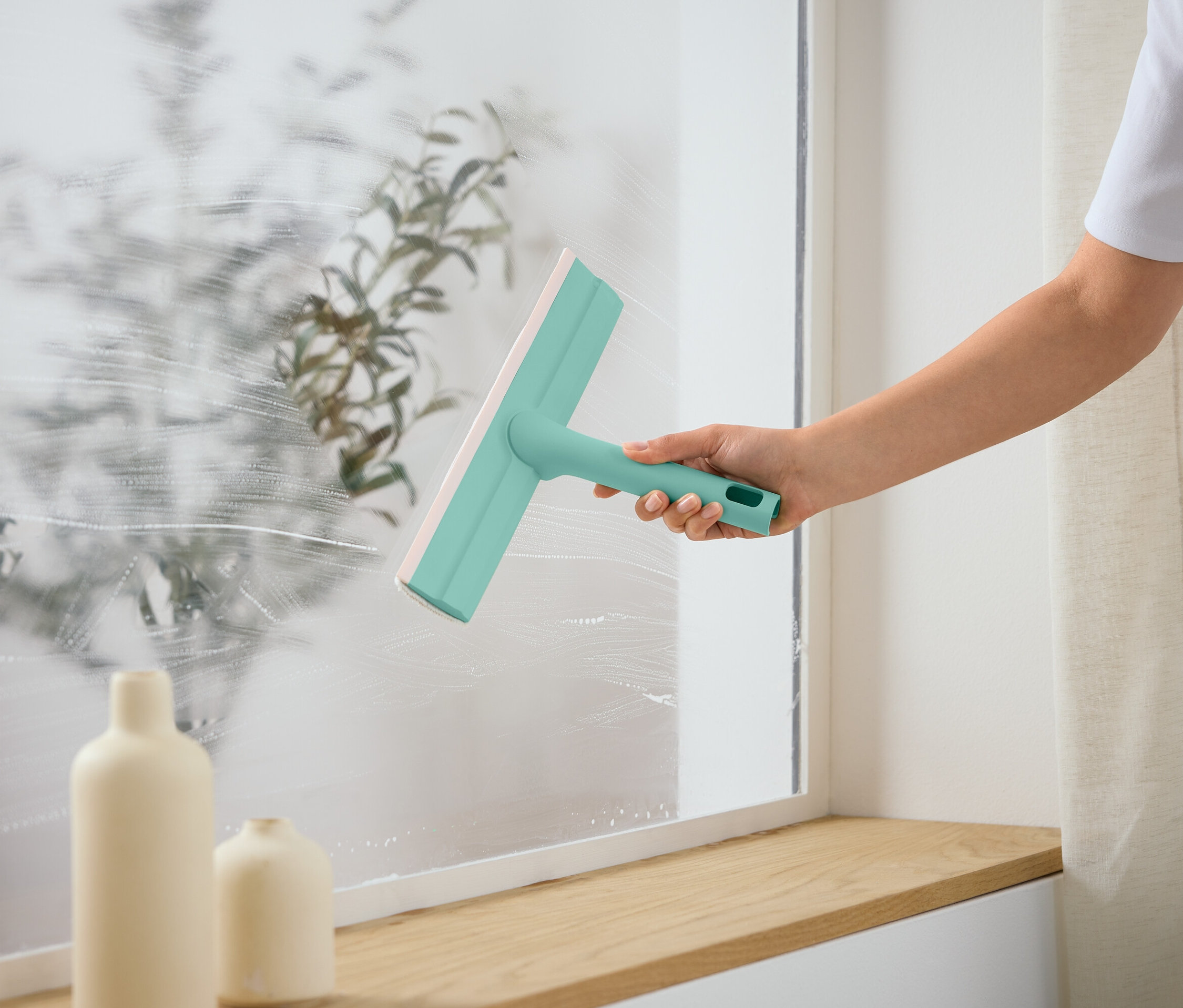 Egy személy ablaktisztítóval tisztít egy ablakot.