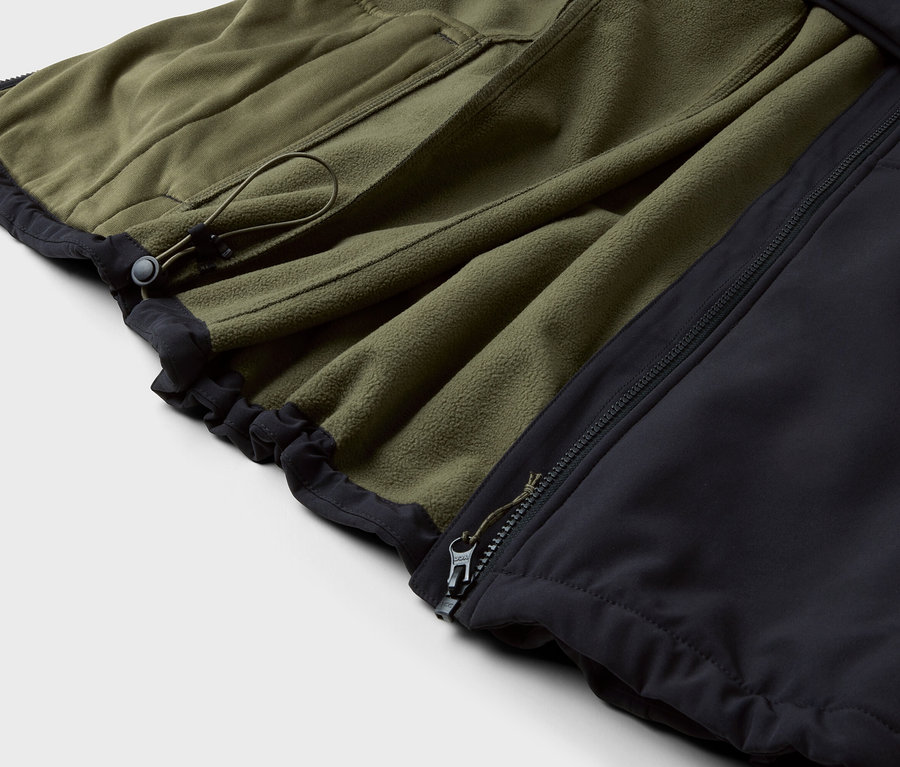 Egy olívazöld polárkabát részlete fekete szegéllyel és cipzárral.