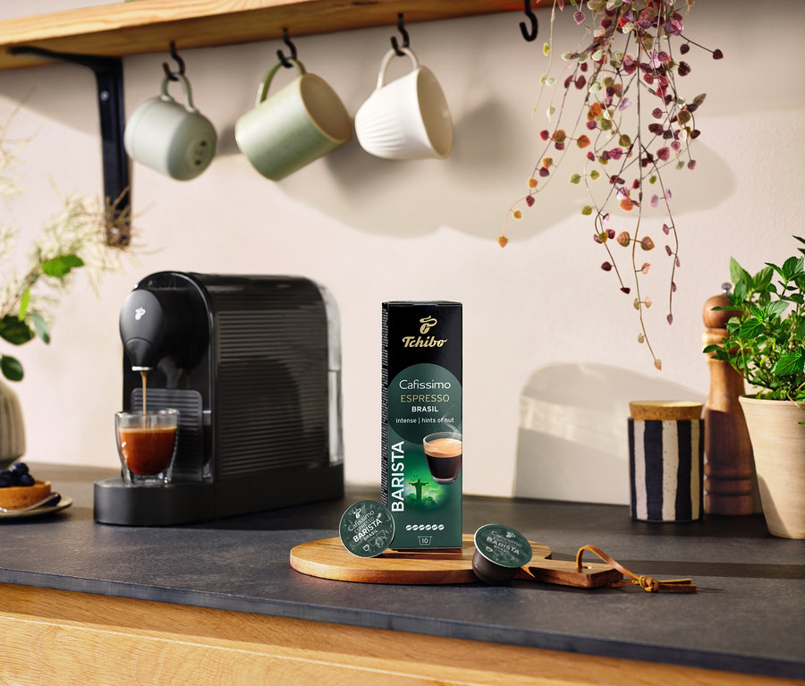 Fekete kávéfőző készít kávét egy pohárba az Espresso Brasil - 10 db kávékapszula csomagolása mellett.