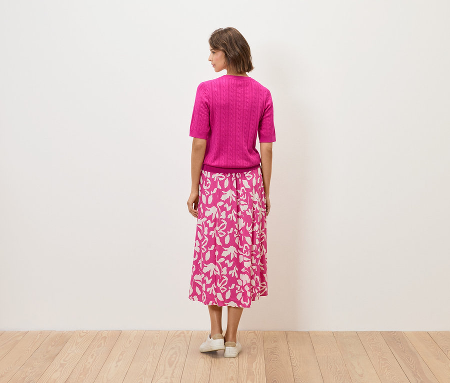 Egy nő háttal áll, rózsaszín felsőt és virágmintás szoknyát visel.