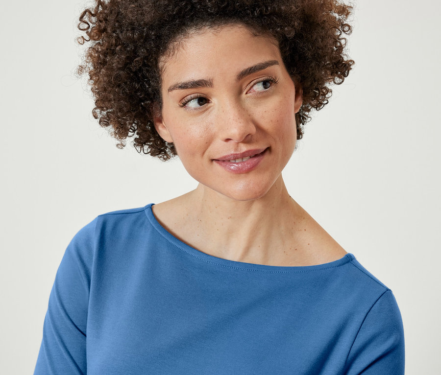 Barna, göndör hajú nő kék, félhosszú ujjú felsőt visel.