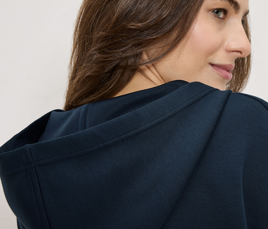 Nő tengerészkék kapucnis pulóvert visel, a válla fölött néz.