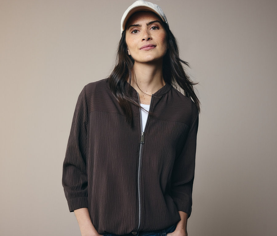 Nő barna kabátban és fehér baseball sapkában.