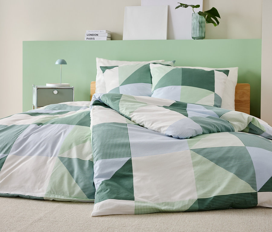 Egy ágy zöld, fehér és kék patchwork takaróval és hozzá illő párnahuzatokkal egy hálószobában.