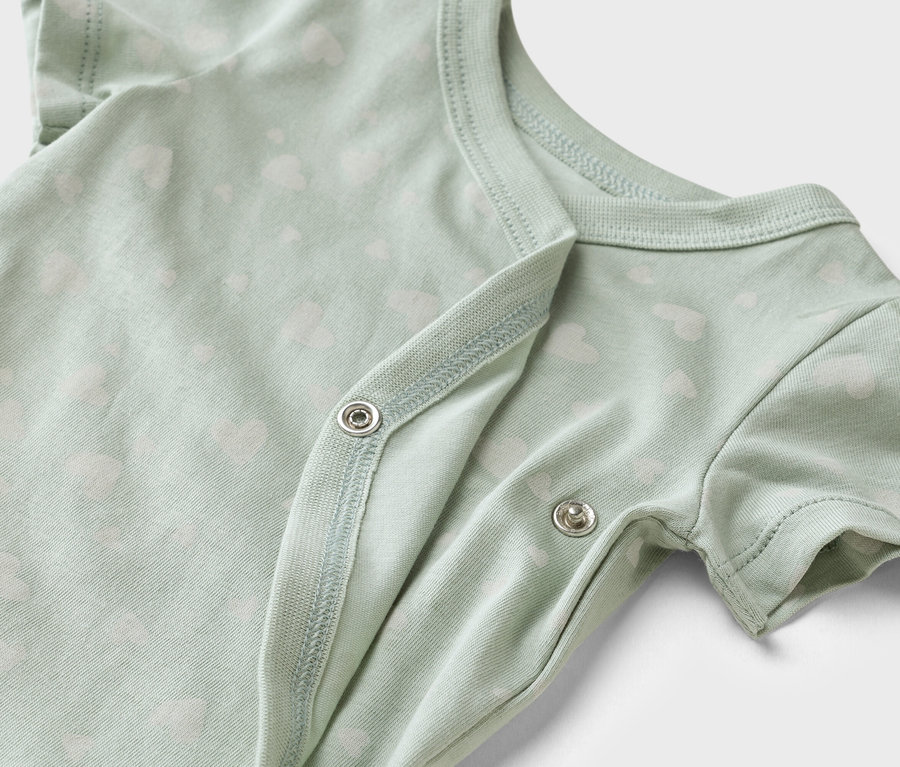 Közeli kép egy világoszöld, szívecskés mintájú, patentos baba body-ról.