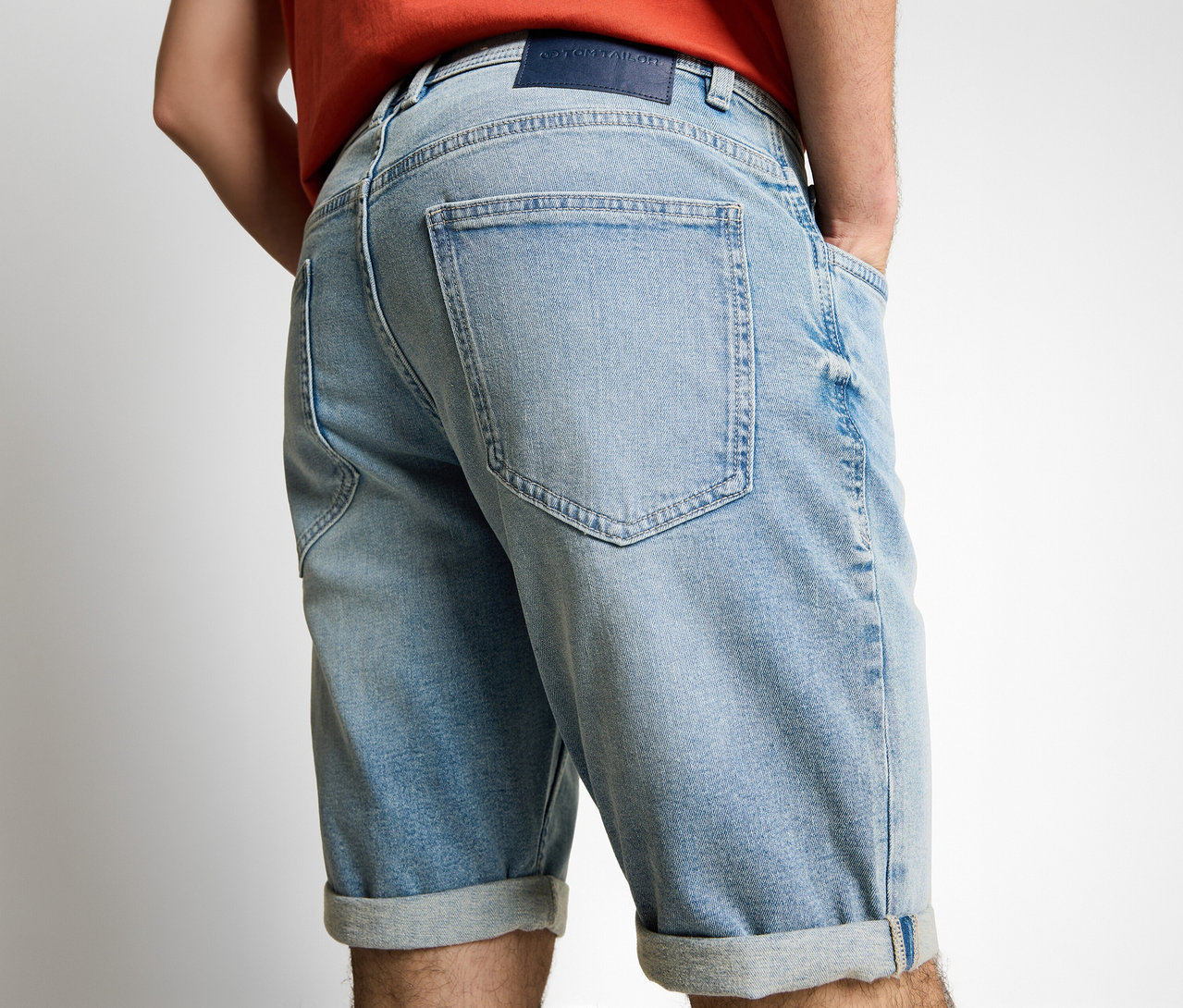 Hátulról látható férfi Tom Tailor TTJOSH REGULAR SLIM farmer rövidnadrágban, kőmosott világoskék denim anyagból, kezével a zsebében.