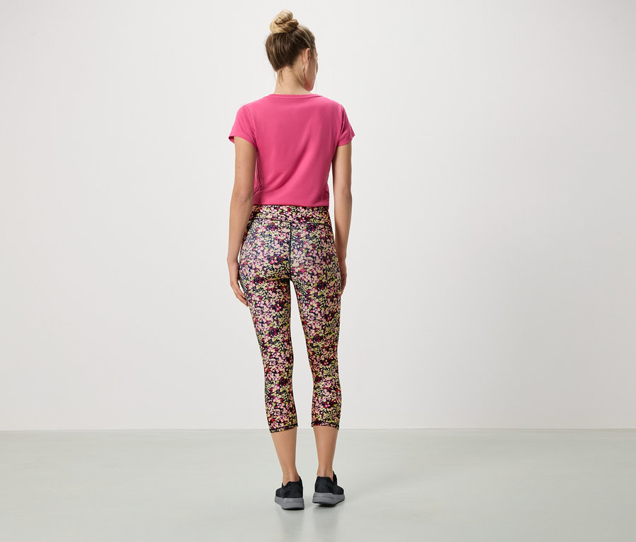 Hátulnézet egy kontyos nőről, aki rózsaszín pólót és virágos leggingset visel.