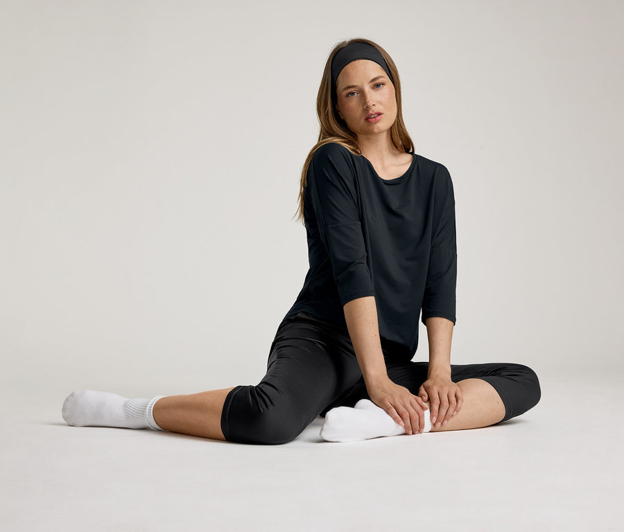 Nő ül fekete 3/4-es sportpólóban. Fejpántot és fehér zoknit visel.