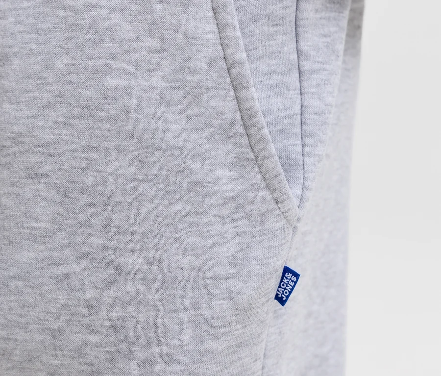 Szürke Jack&Jones Bradley szabadidőnadrág közeli felvétele, melyen látszik az anyag textúrája, egy oldalzseb és egy kék Jack&Jones címke.