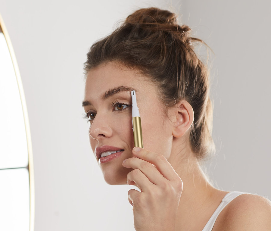 Nő igazítja a szemöldökét elektromos szemöldökformázóval.