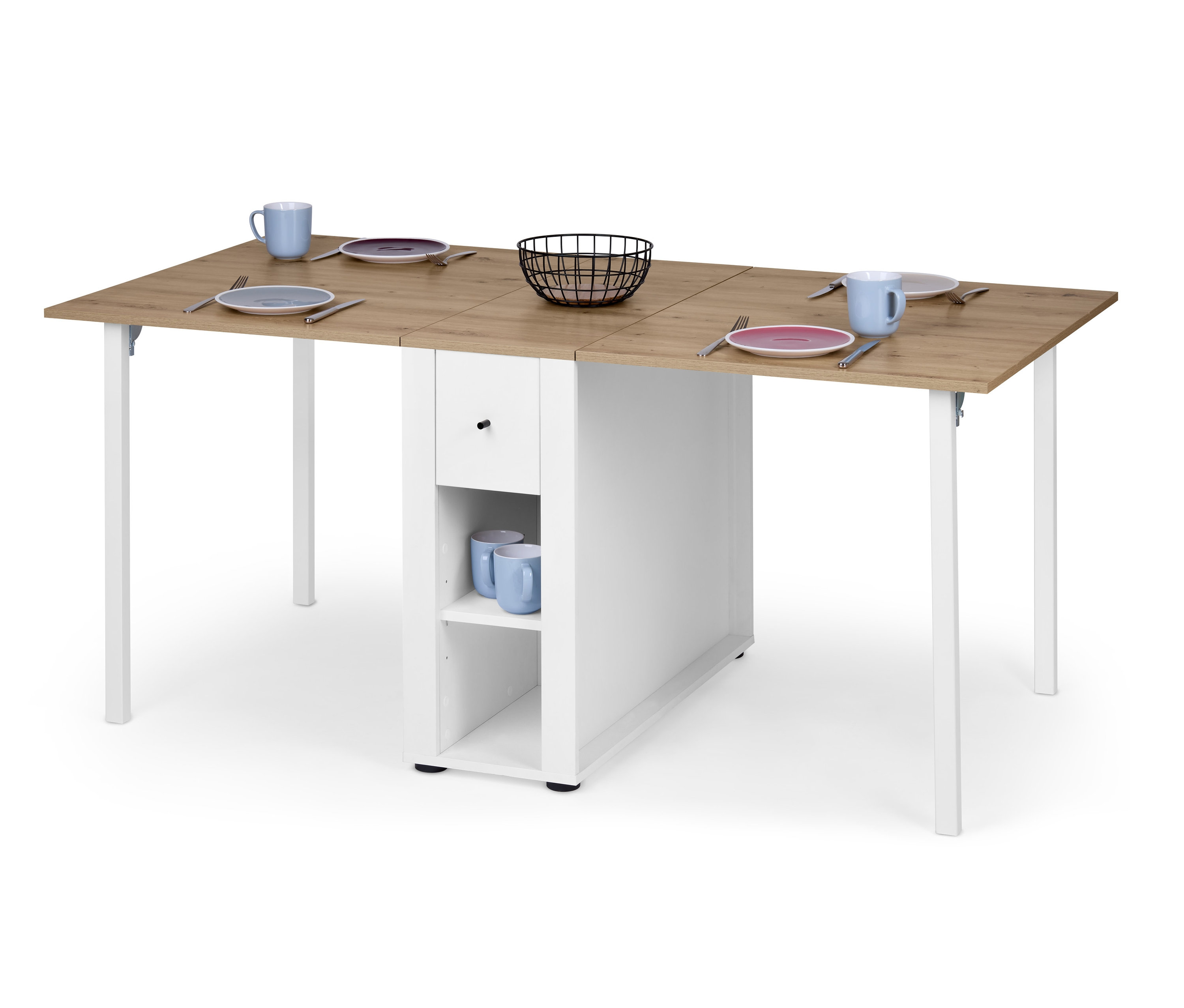 Felnyitható asztal, tárolóval, tölgy/fehér színben, rajta tányérok, evőeszközök, bögrék és egy kosár.