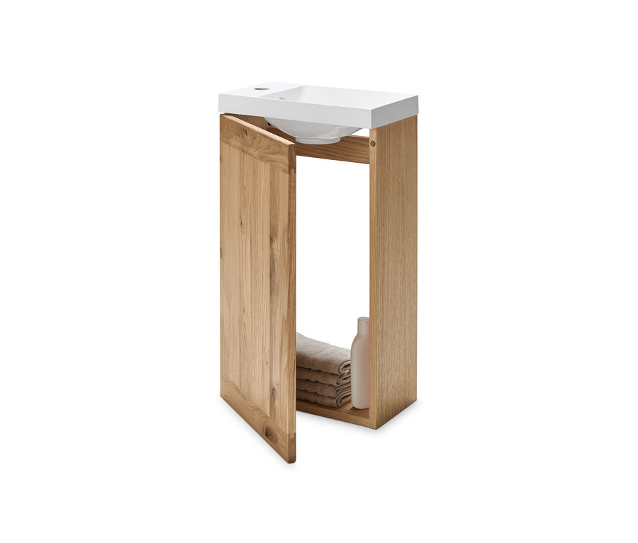 Kis méretű alsó szekrény mosdóval, nyitott ajtóval, belül összehajtott törölközőkkel és egy flakonnal.