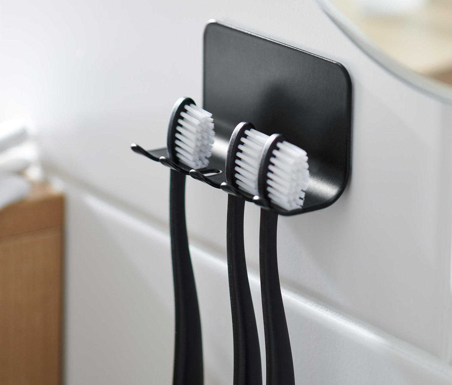 Fekete fogkefetartó három fogkefével fehér csempén.