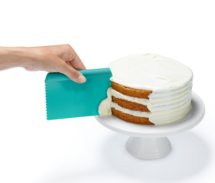 Egy kéz mázat ken egy háromrétegű tortára a 3 sütési segédeszköz egyikével, egy türkiz spatulával.