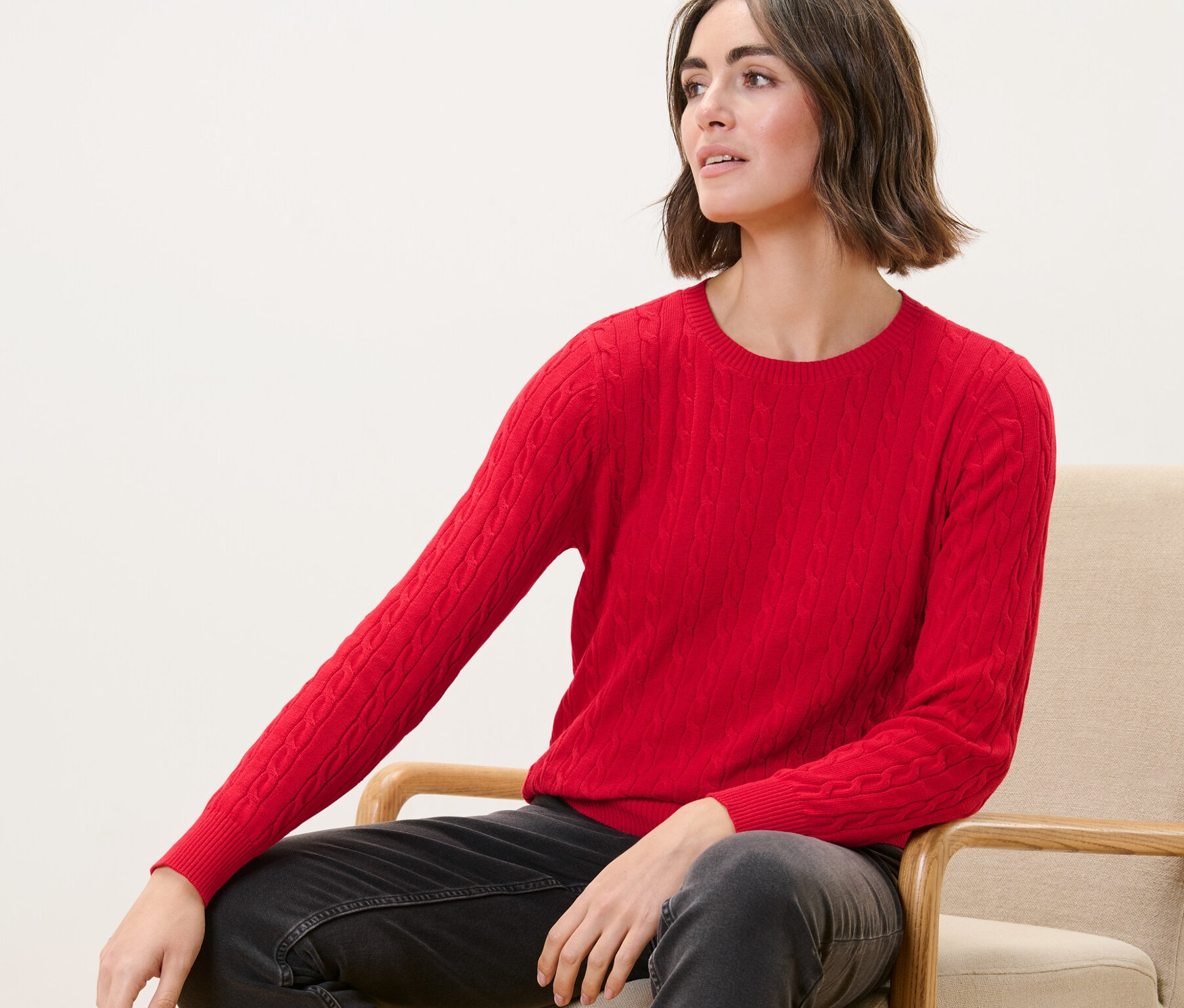 Egy nő egy székben ül, és egy piros, fonott mintás kötött pulóvert visel.