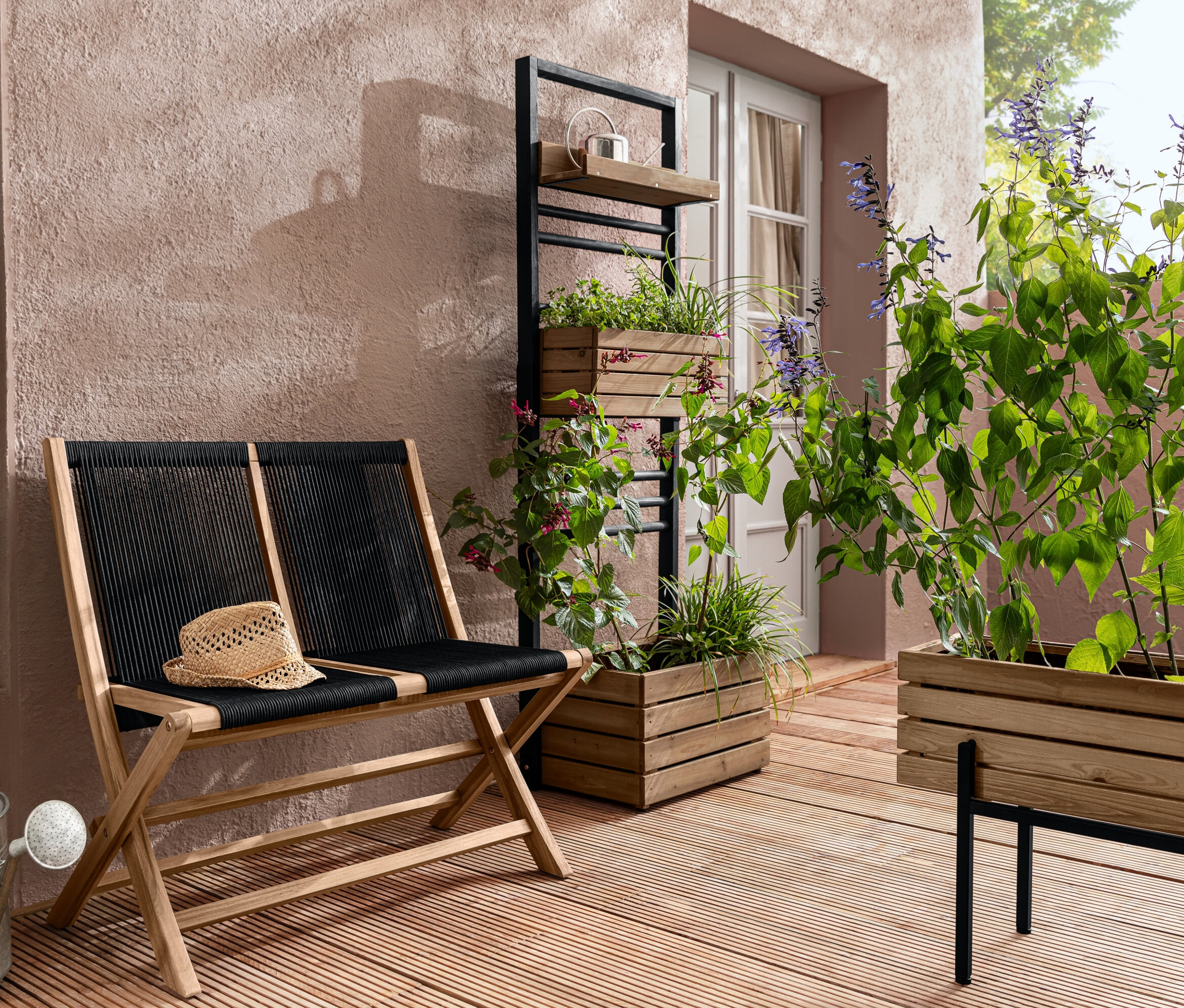 Egy összecsukható kerti pad textilhálóval, egy »Elin« ültetőládás fal és egy »Elin« ültetőláda növényekkel egy teraszon.