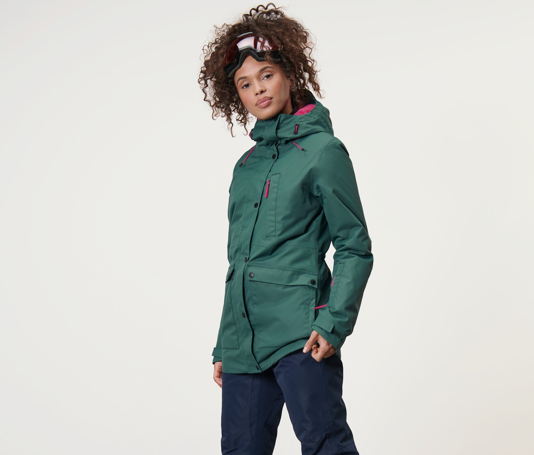 Nő visel sötétzöld sí- és snowboard kabátot és sínadrágot.