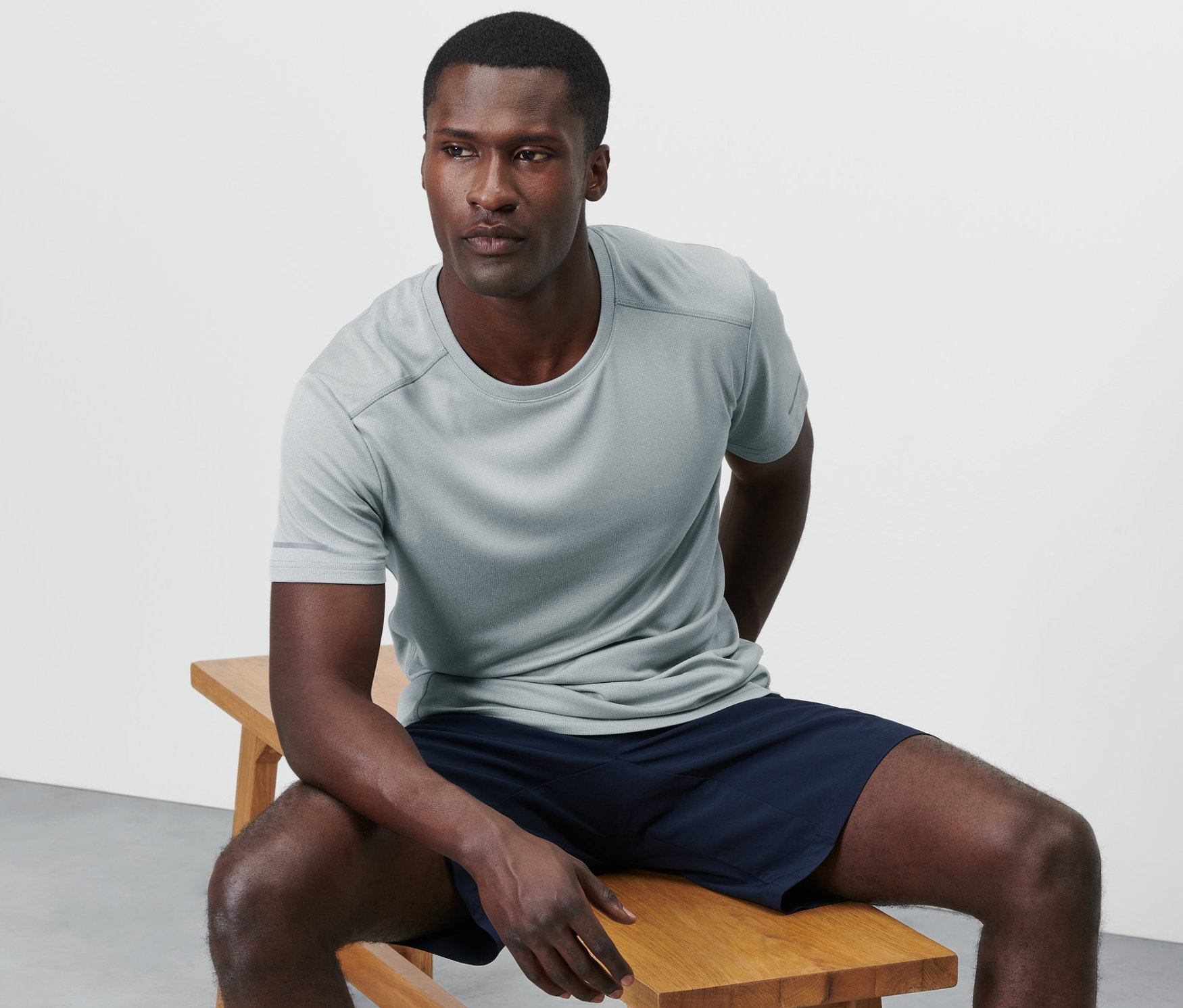 Egy férfi ül egy fa padon, melírozott szürke funkcionális felsőt visel.