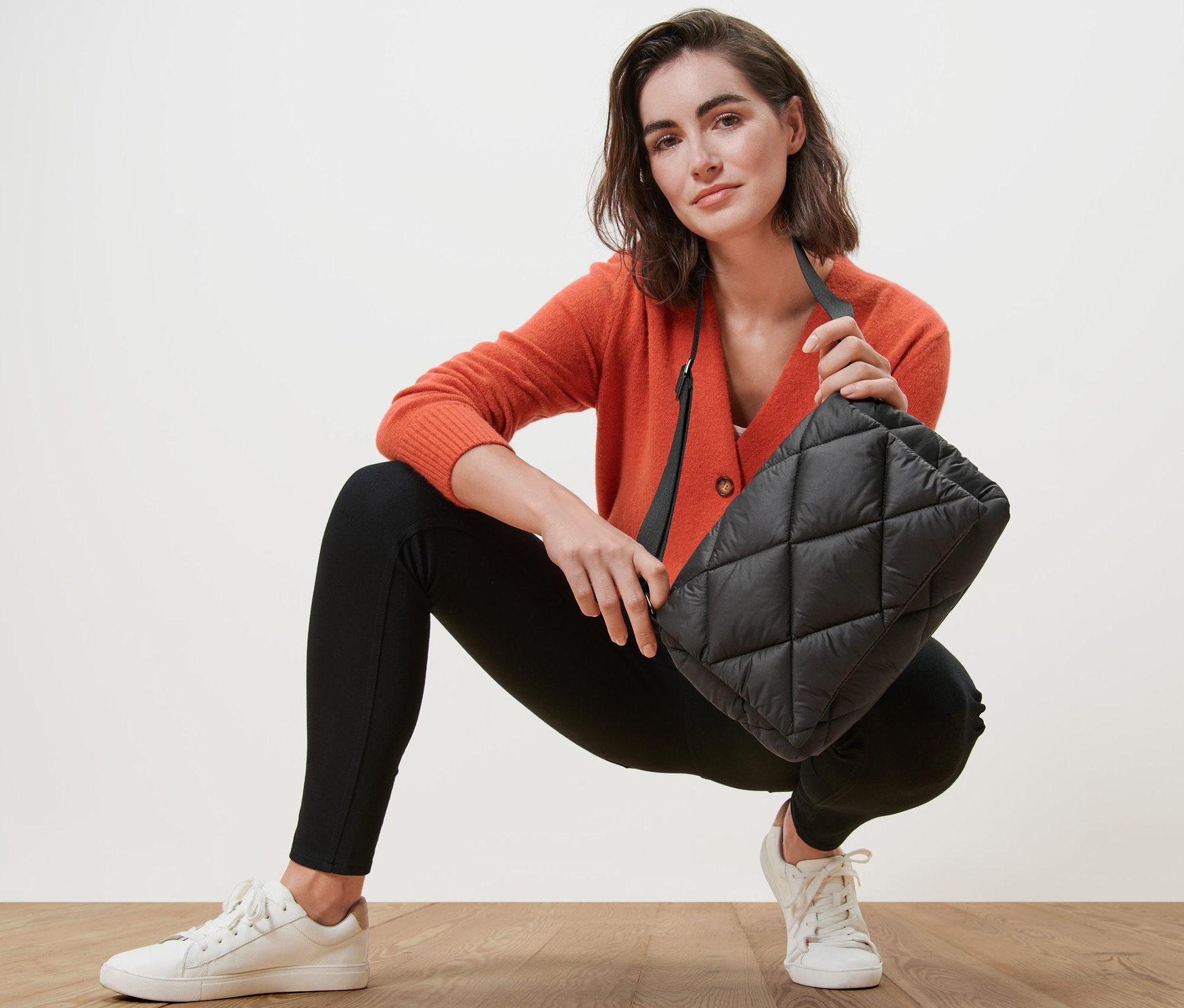 Narancssárga kardigánt viselő nő steppelt oldaltáskát tart.