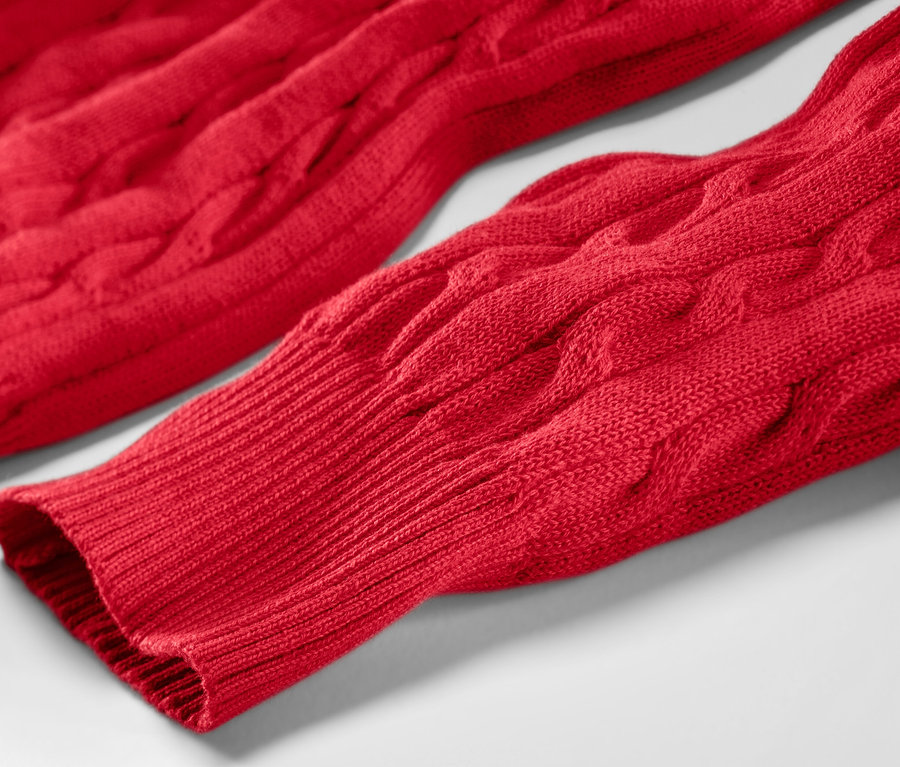 Egy piros, fonott mintás kötött pulóver részlete.