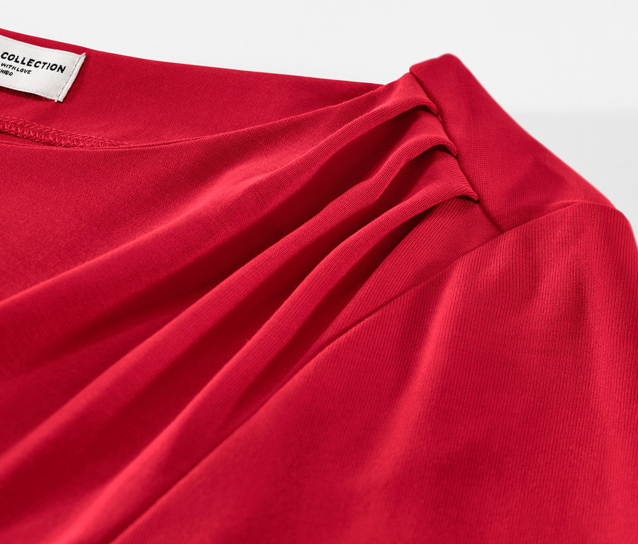 Egy piros, ráncolt női hosszú ujjú pólóblúz részlete.