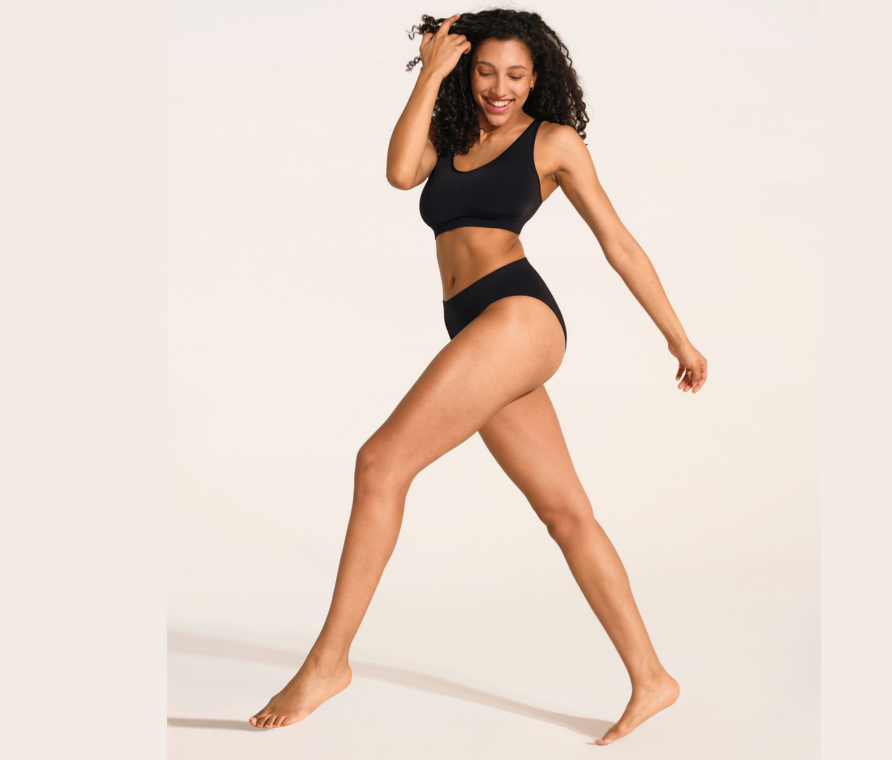 Egy nő sétál és mosolyog, fekete SCHIESSER puha melltartót és fekete SCHIESSER Rió fazonú alsót visel.