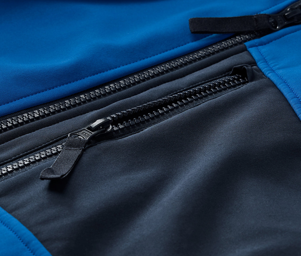 Kék-fekete softshell dzseki részlete cipzárakkal.