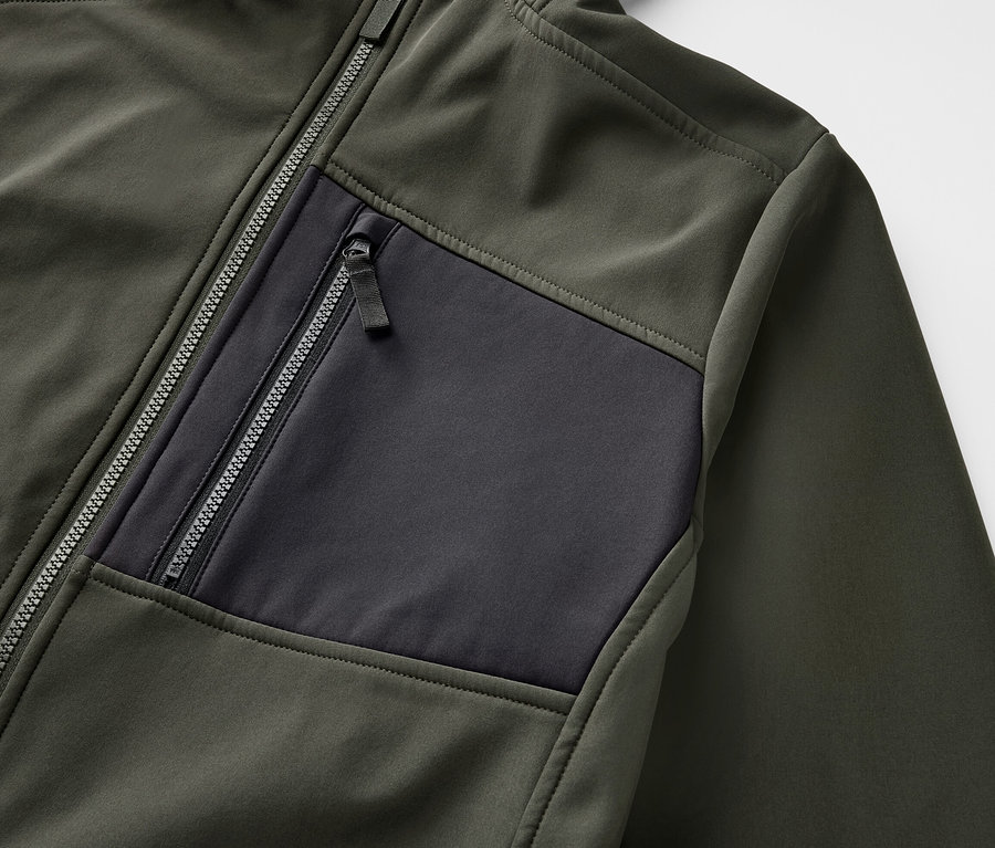 Egy khaki softshell dzseki részlete, cipzárral és fekete zsebbel.