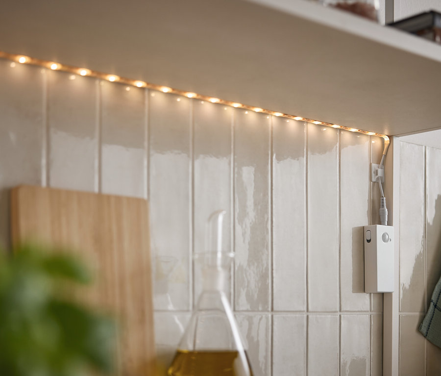 LED szalag világít a szekrény alatt fehér csempéken.