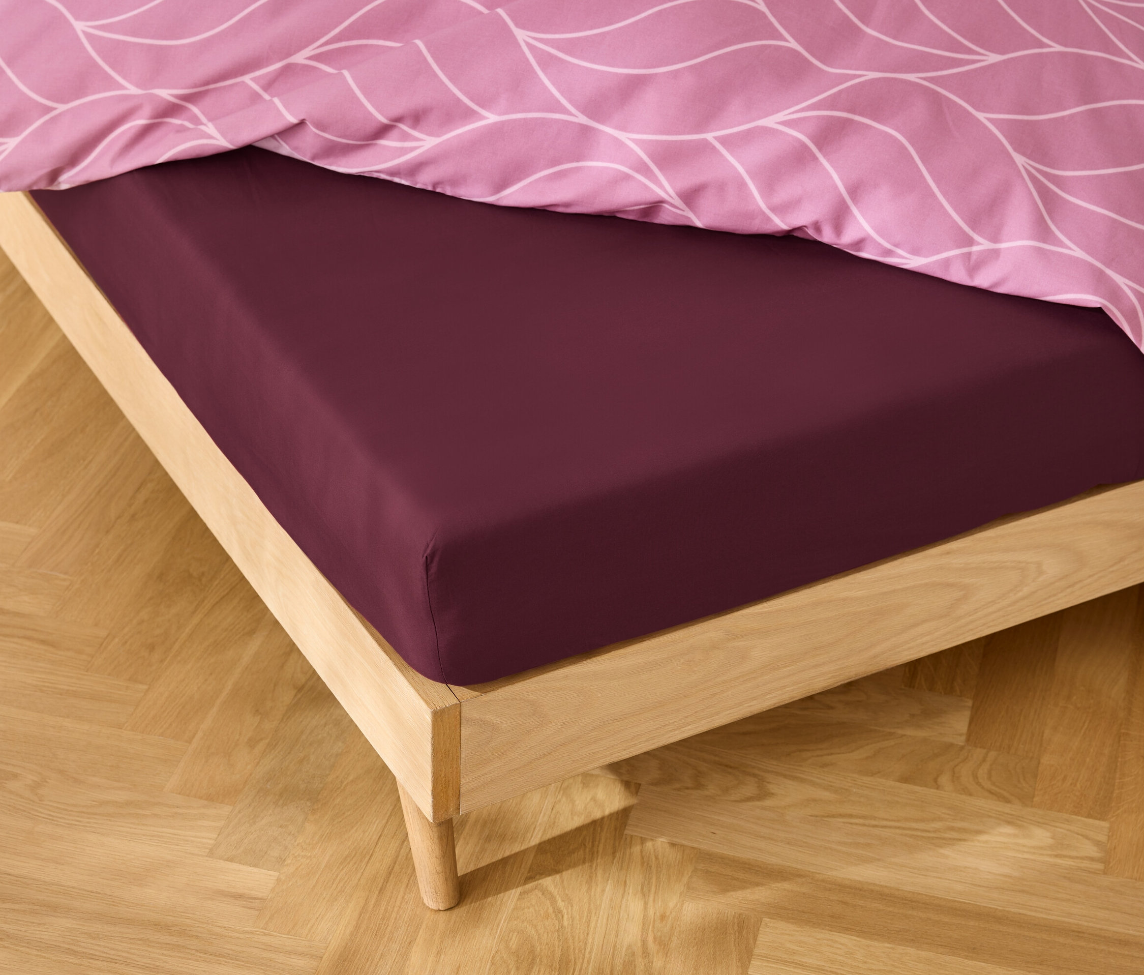 Egy ágy közeli képe bordó lepedővel és rózsaszín, mintás ágyneművel.