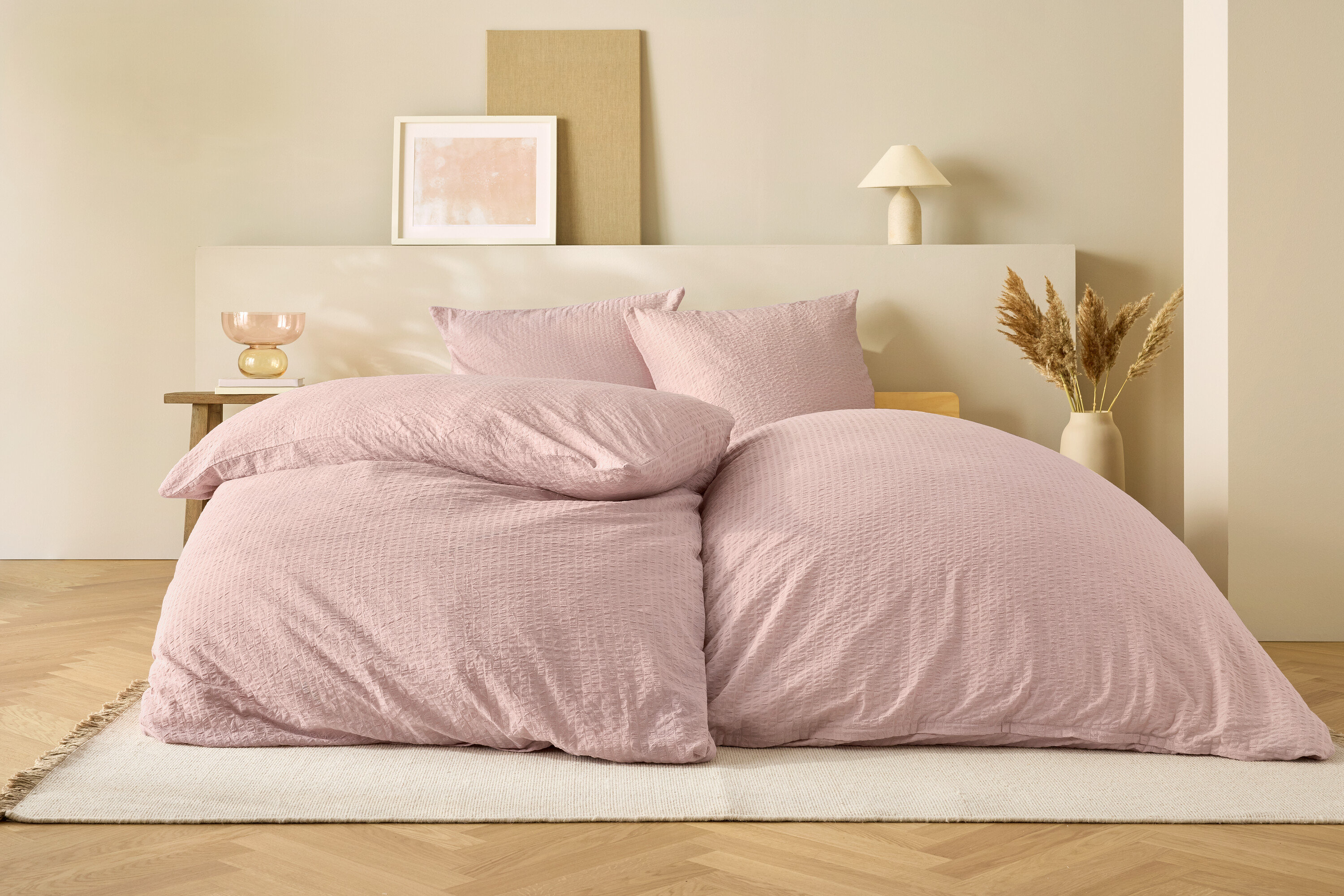 Rózsaszín ágynemű egy ágyon, bézs háttérrel.