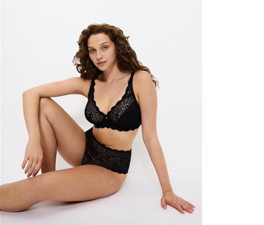 Nő ül a földön, fekete csipkés melltartót és bugyit visel.