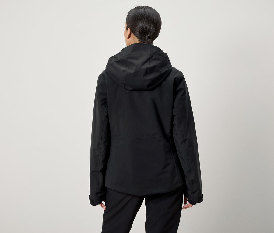 Hátulról látható egy lófarokba kötött hajú nő, aki fekete kapucnis kabátot és fekete nadrágot visel.