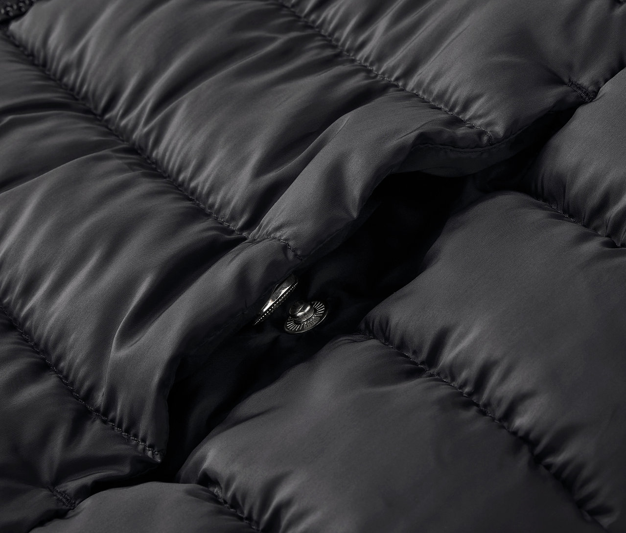 Egy fekete, steppelt kabát részlete, patenttal.