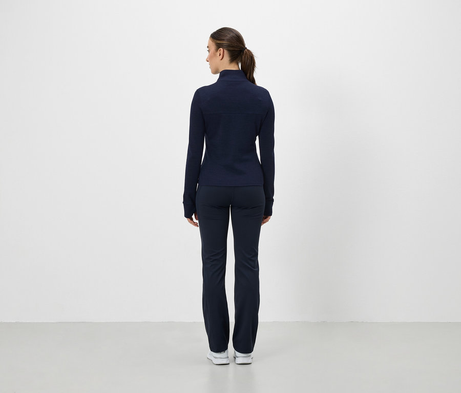 Egy nő háttal a kamerának, sötétkék sportdzsekit és nadrágot visel.