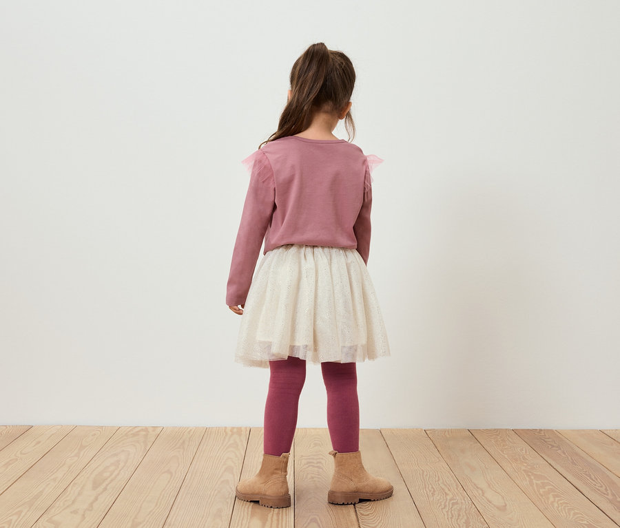 Hátulról látható kislány rózsaszín pulóvert, csillogó szoknyát, rózsaszín leggingset és barna csizmát visel.