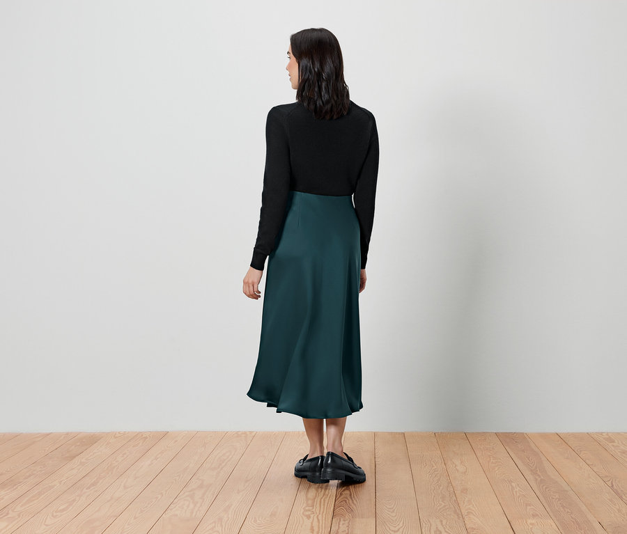 Egy nő háttal áll, fekete felsőt és zöld szoknyát visel.