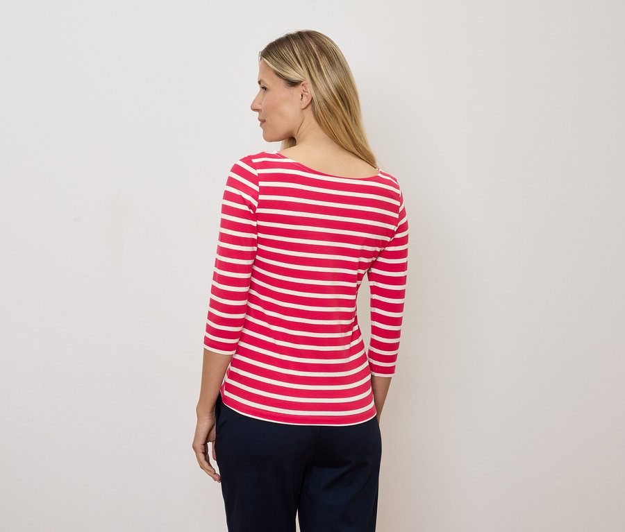 Egy szőke nő balra néz, és egy piros-fehér csíkos, háromnegyedes ujjú pólót visel.
