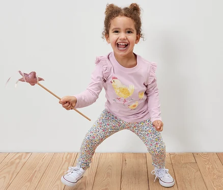 Mosolygó kislány varázspálcát tart, és rózsaszín 2 kislány leggings, virágos leggingset és csirkés mintás pólót visel.
