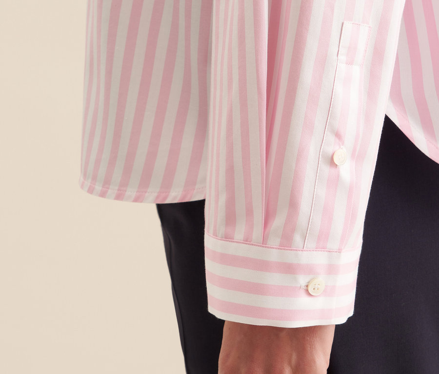 Egy rózsaszín, fehér csíkos Seidensticker oversize női ingblúz részlete egy nő karján.