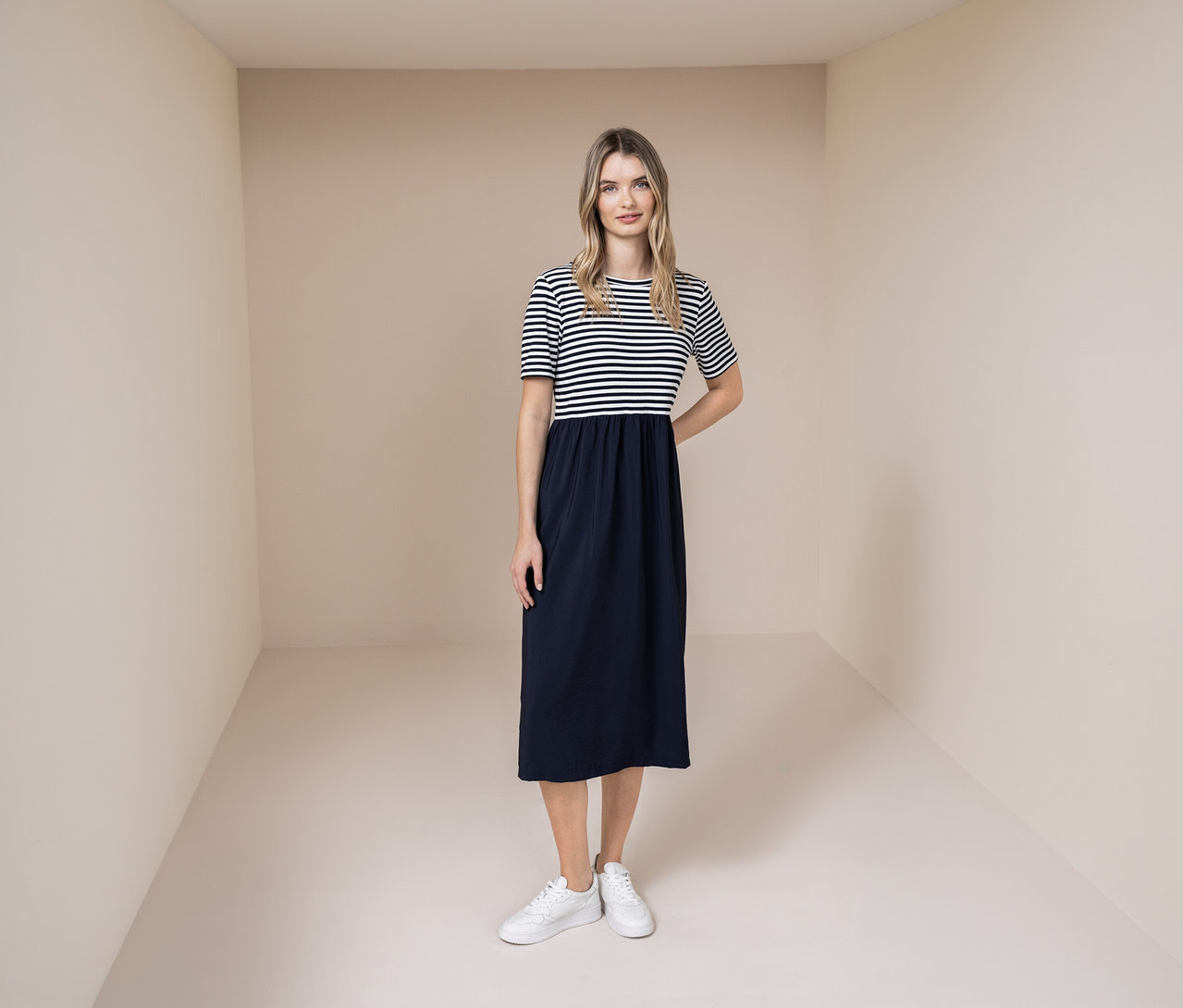 Nő Street One ruhában, kék-fehér csíkos felsőrésszel és kék szoknyával, valamint fehér tornacipőben.