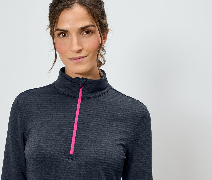 A nő egy sötétkék, hosszú ujjú felsőt visel, rózsaszín cipzárral.