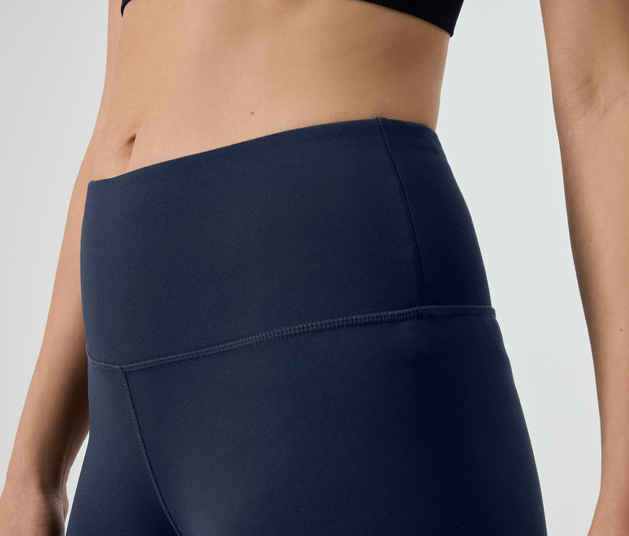 Közeli kép egy sötétkék leggingset és fekete sportmelltartót viselő nőről.