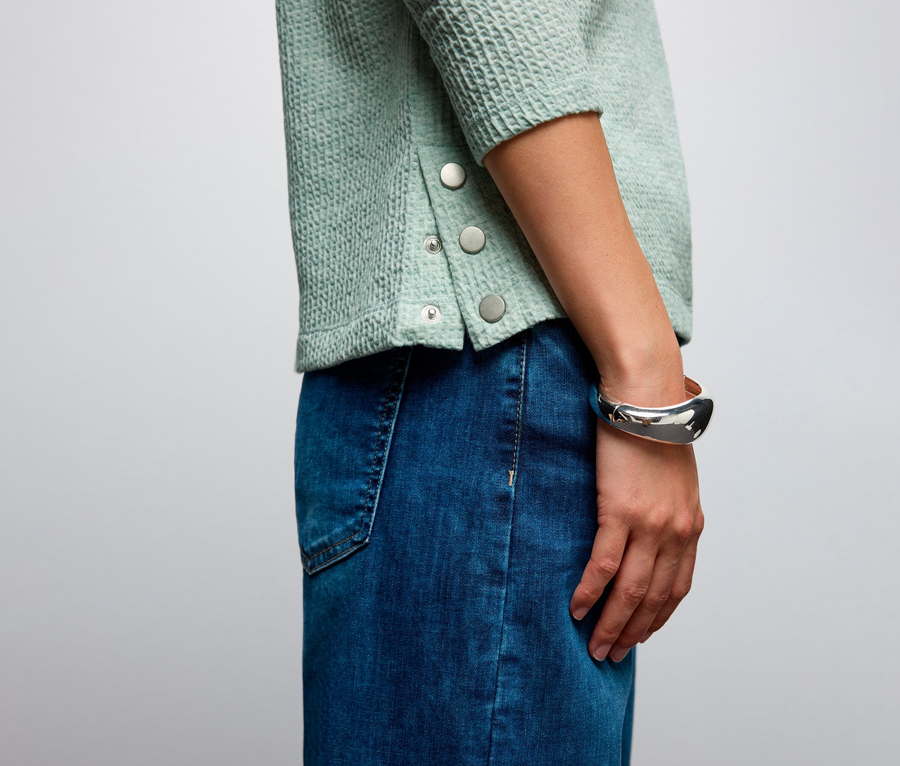 Egy nő közeli képe Street One bordás mintás pólóban és farmer szoknyában.